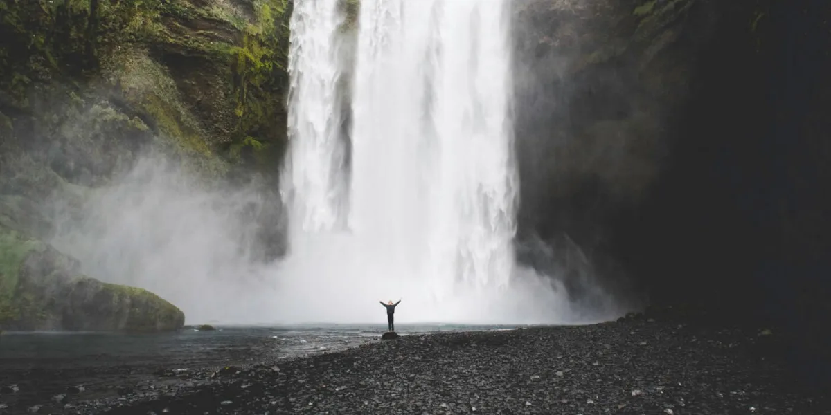 A huge waterfall in the background and a small figure standing at the bottom, raising their arms.